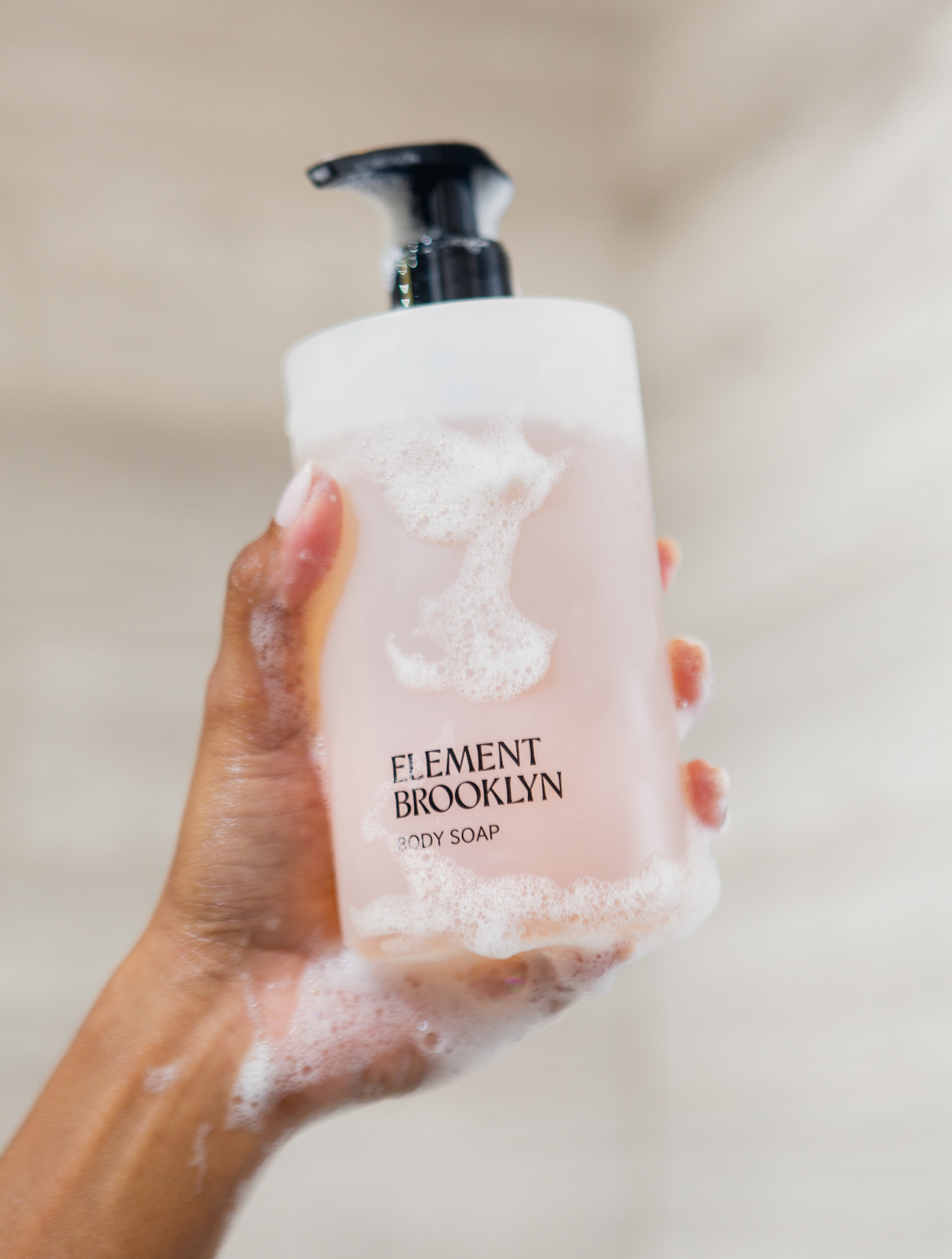 A hand holding a bottle of Element Brooklyn liquid soap with white foam
