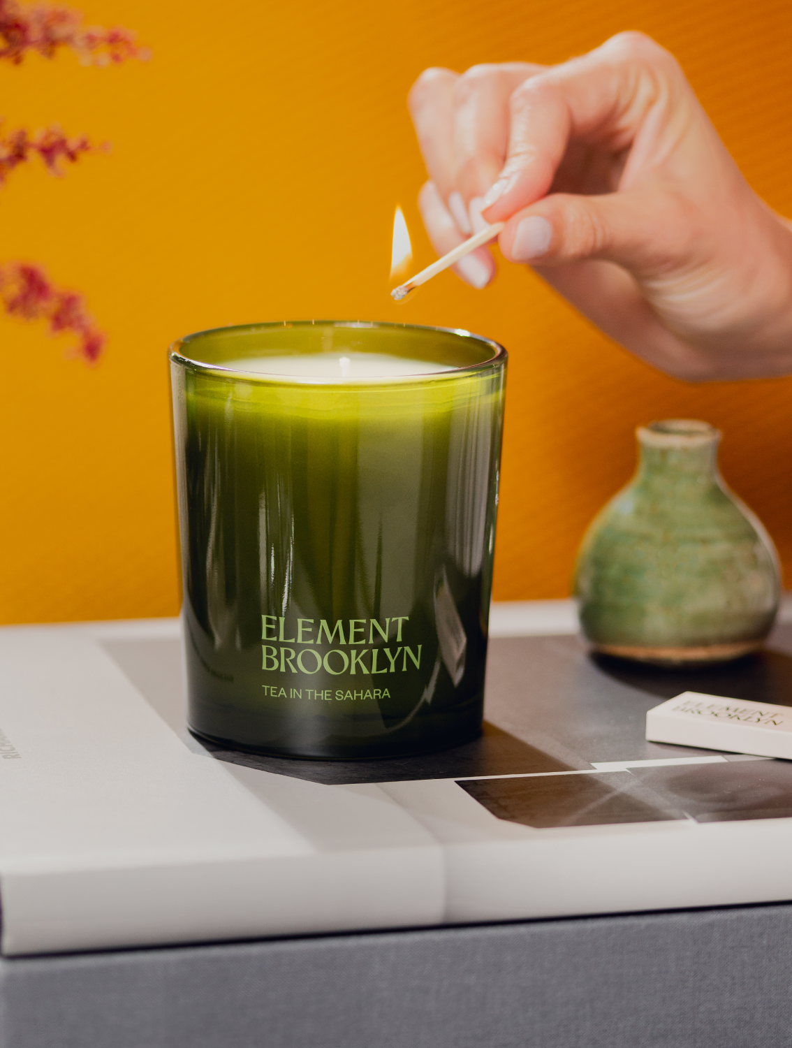 A hand lighting an Element Brooklyn candle with decorative items in the background