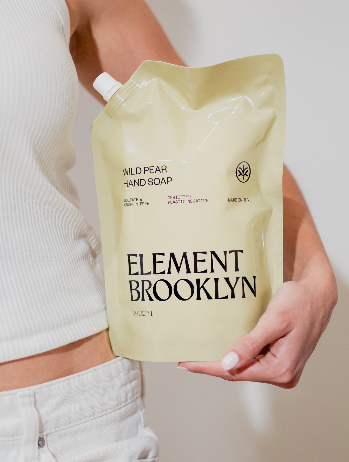 A person holding a refill pouch of Element Brooklyn liquid hand soap with wild pear scent